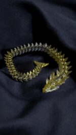 Bracelet 3D imprimé en plastique avec design or et argent, élégant et moderne, posé sur un tissu noir foncé.