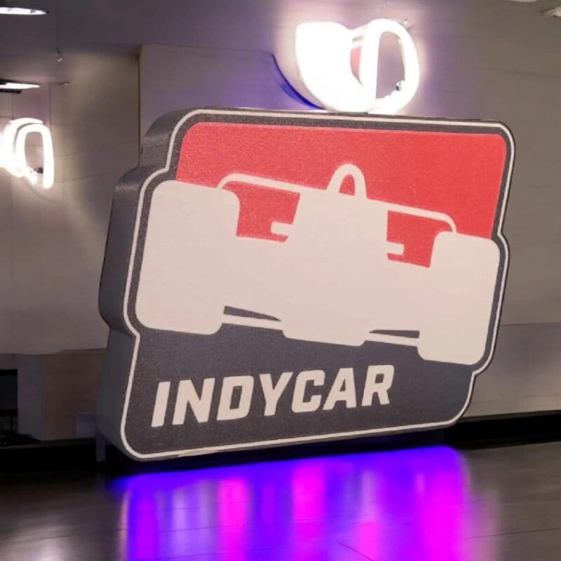 LED lumineuse en forme de panneau de course automobile avec inscription "INDYCAR" en 3D, créant une ambiance moderne et sportive dans un espace intérieur.
