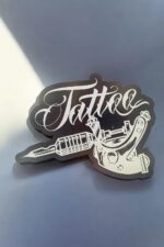 L'accessoire décoratif en acrylique avec inscription "Tattoo" et motif de machine à tatouer, idéal pour la décoration ou comme cadeau personnalisé.