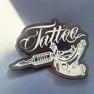 L'accessoire décoratif en acrylique avec inscription "Tattoo" et motif de machine à tatouer, idéal pour la décoration ou comme cadeau personnalisé.
