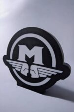 Sculpture lumineuse 3D représentant un logo design avec lettres "M" et ailes stylisées, réalisée en matériaux d'impression 3D, idéale pour décoration ou luminaire LED.