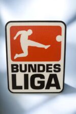 Panneau lumineux avec silhouette de joueur de football en coup de pied, logo de la BundesLiga, création lumineuse 3D, lampe LED design sportif, décoration moderne, fabrication Française, art lumineux 3D pour fans de football et collectionneur.