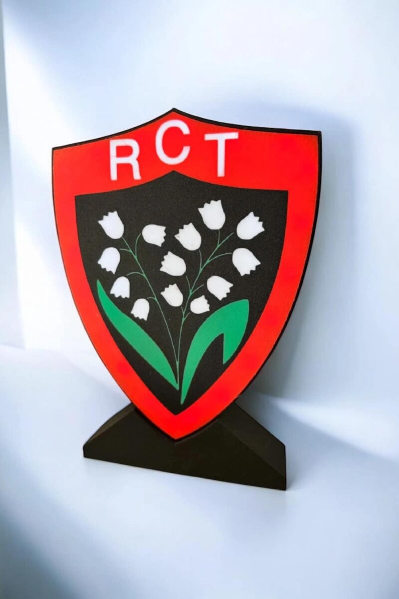 Lampe LED 3D représentant un bouclier rouge avec un logo floral et les lettres "RCT", créant une décoration lumineuse unique pour l'intérieur ou extérieur.