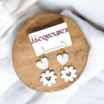 Boucles d'oreilles en forme de cœurs et fleurs en acrylique blanc avec accents dorés, créées avec impression 3D, présentées sur un support en bois, dans l'esprit des créations lumineuses 3D d'Infinity 3D Print.