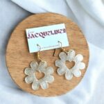 Boucles d'oreilles en plastique transparent en forme de fleur avec cœur central, montées sur welded or, posées sur un fond de bois, créant un effet lumineux 3D pour un style élégant et original.