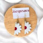 Bracelets fantaisie en plastique blanc avec détails rouges en forme de fleurs, montés sur boucles d'oreilles dorées. Parfait pour un style original et coloré.