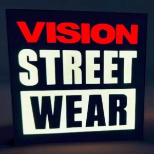 Vitrine lumineuse LED affichant le message "VISION STREET WEAR" avec éclairage en flip-flop rouge, blanc et noir, idéale pour décoration intérieure ou publicité vintage.