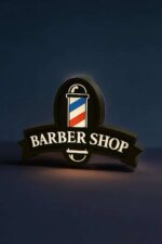 Barbier logo lumineux en 3D avec éclairage LED, représentant un pistolet de barbier classique, idéal pour une ambiance moderne et artistique dans un salon de coiffure ou barbershop.