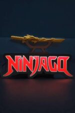 L’image montre une lampe LED en forme de logo Ninjago 3D, illuminée en rouge, avec une épée ninja en décoration située au-dessus. La lampe est posée sur une surface sombre, créant un effet visuel dynamique et moderne.